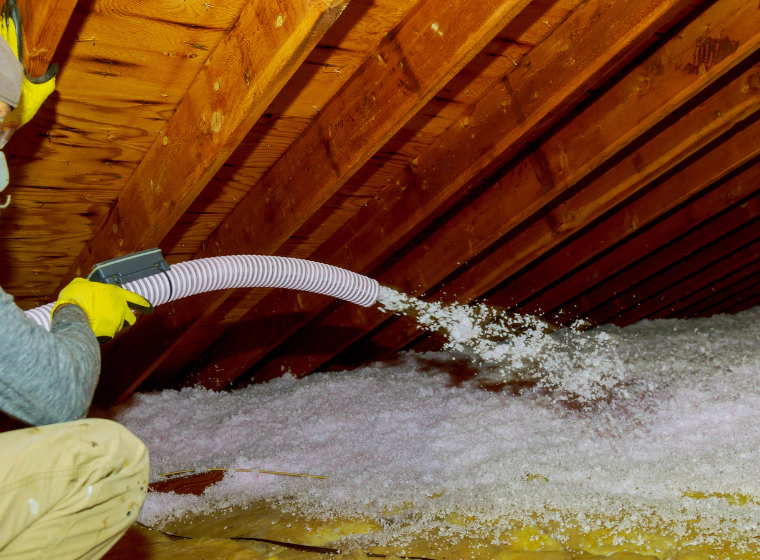 spraying blown fiberglass insulation in the attic